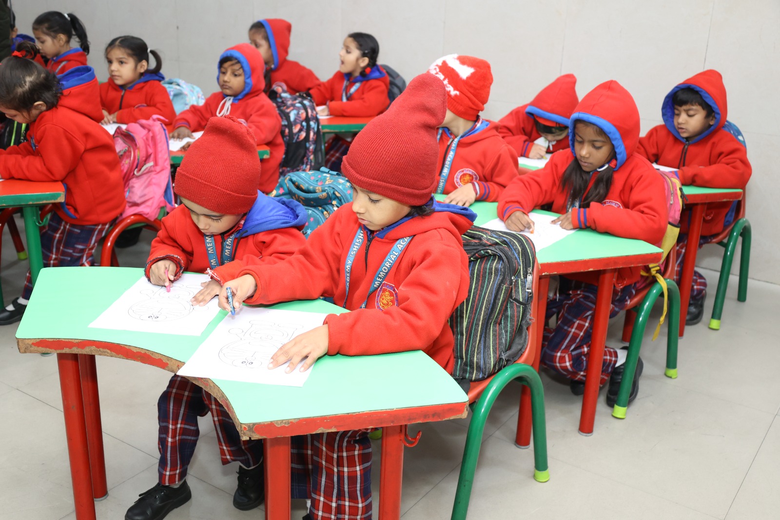 Pre-primary children in red winter jackets colouring at their desks