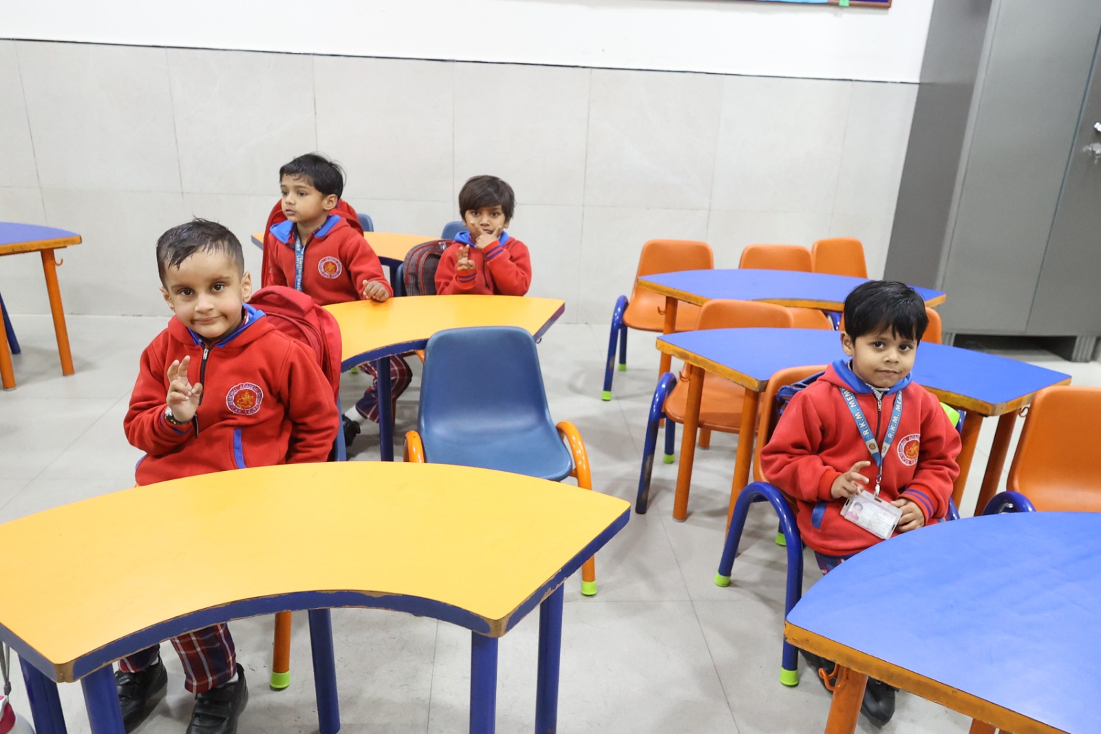 Three young children seated at curved orange and blue tables, smiling at the camera