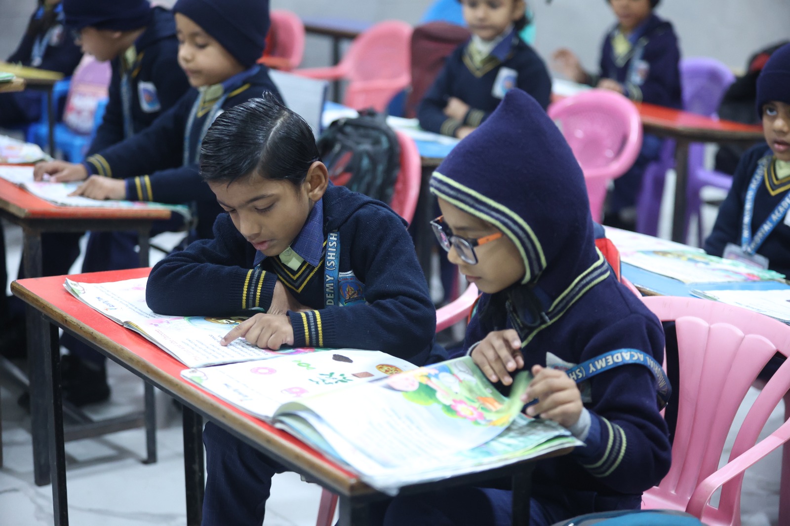 Pair of young students reading their workbooks at colourful desks