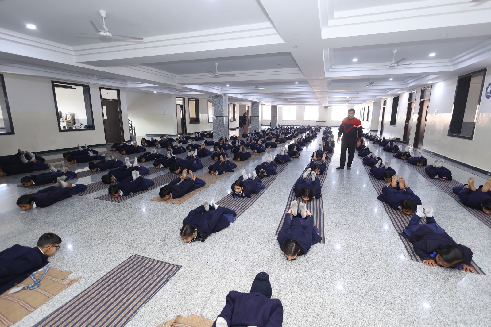 Children practising plough pose on striped mats in the yoga hall